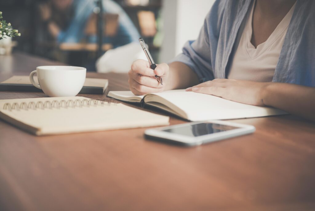 Woman writing on a notebook beside teacup and tablet computer